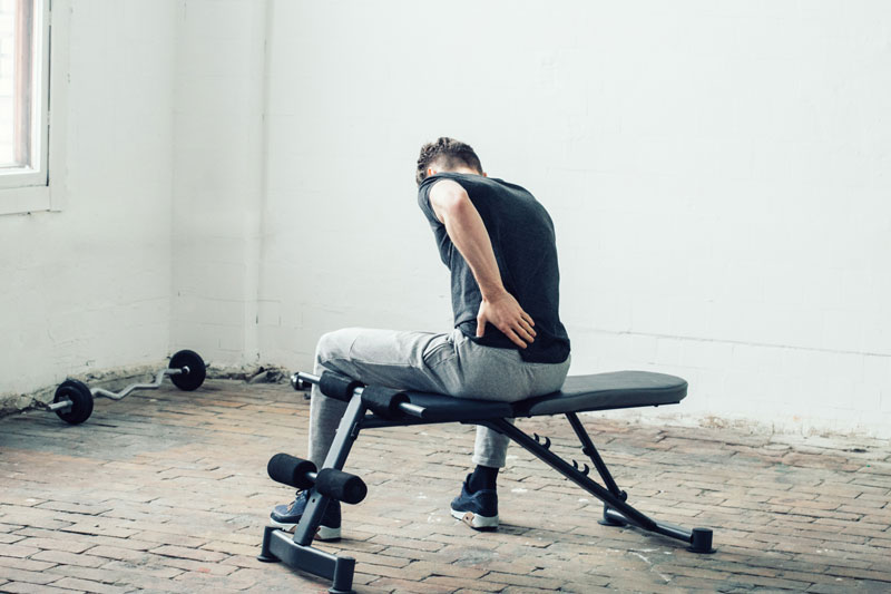Man is sat on exercise bench with sore back