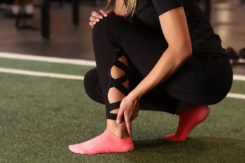Woman wearing dance or yoga attire is holding her ankle in pain